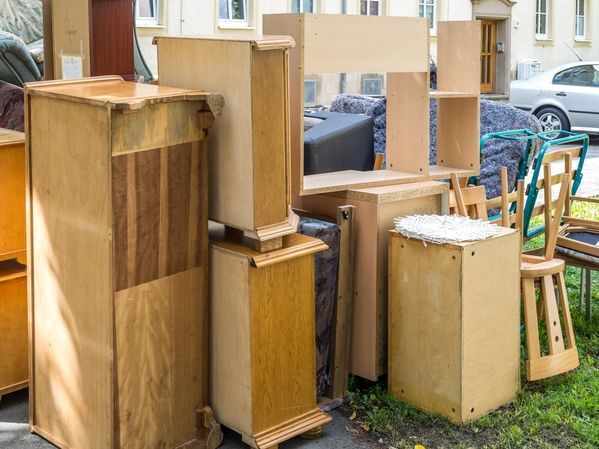 Verschiedene alte Holzmöbelstücke und ein blauer Handwagen auf einem Bürgersteig vor Wohnhäusern
