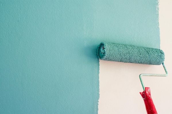 Farbrolle mit türkisfarbener Farbe beim Streichen einer Wand